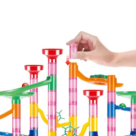 Main assemblant les éléments du circuit à billes Billitrack avec tubes transparents et pièces colorées