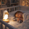 Bébé endormi dans son lit avec veilleuse toucan LumaTouco diffusant une lumière douce apaisante